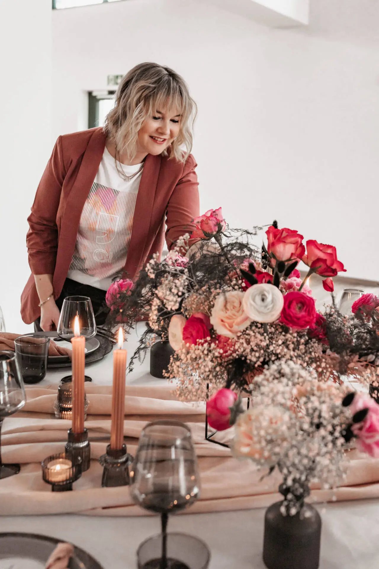 Frau dekoriert Tisch mit Blumen und Kerzen.