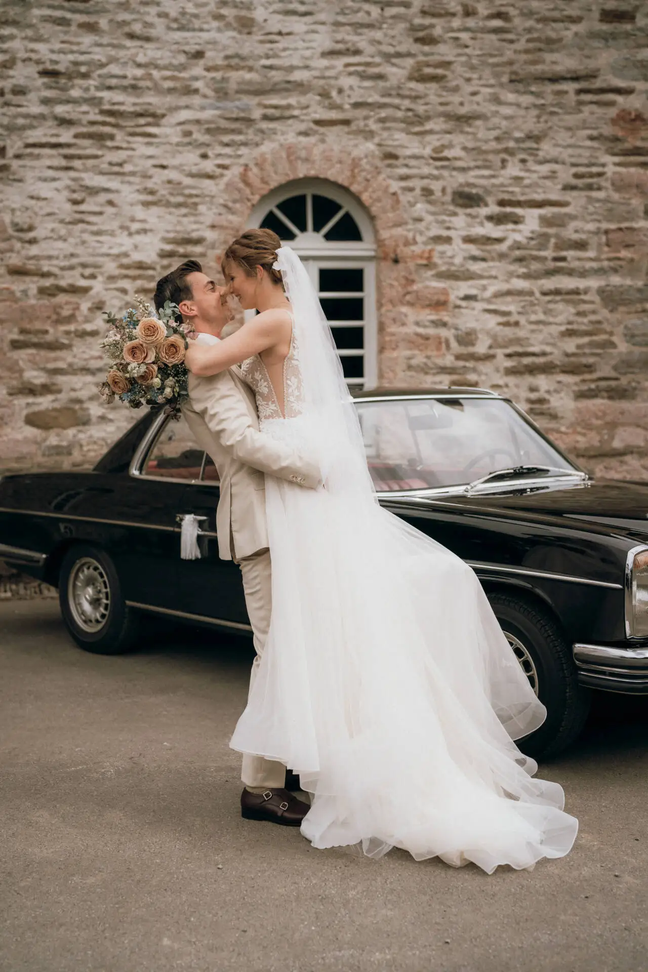 Brautpaar umarmt sich vor einem Oldtimer