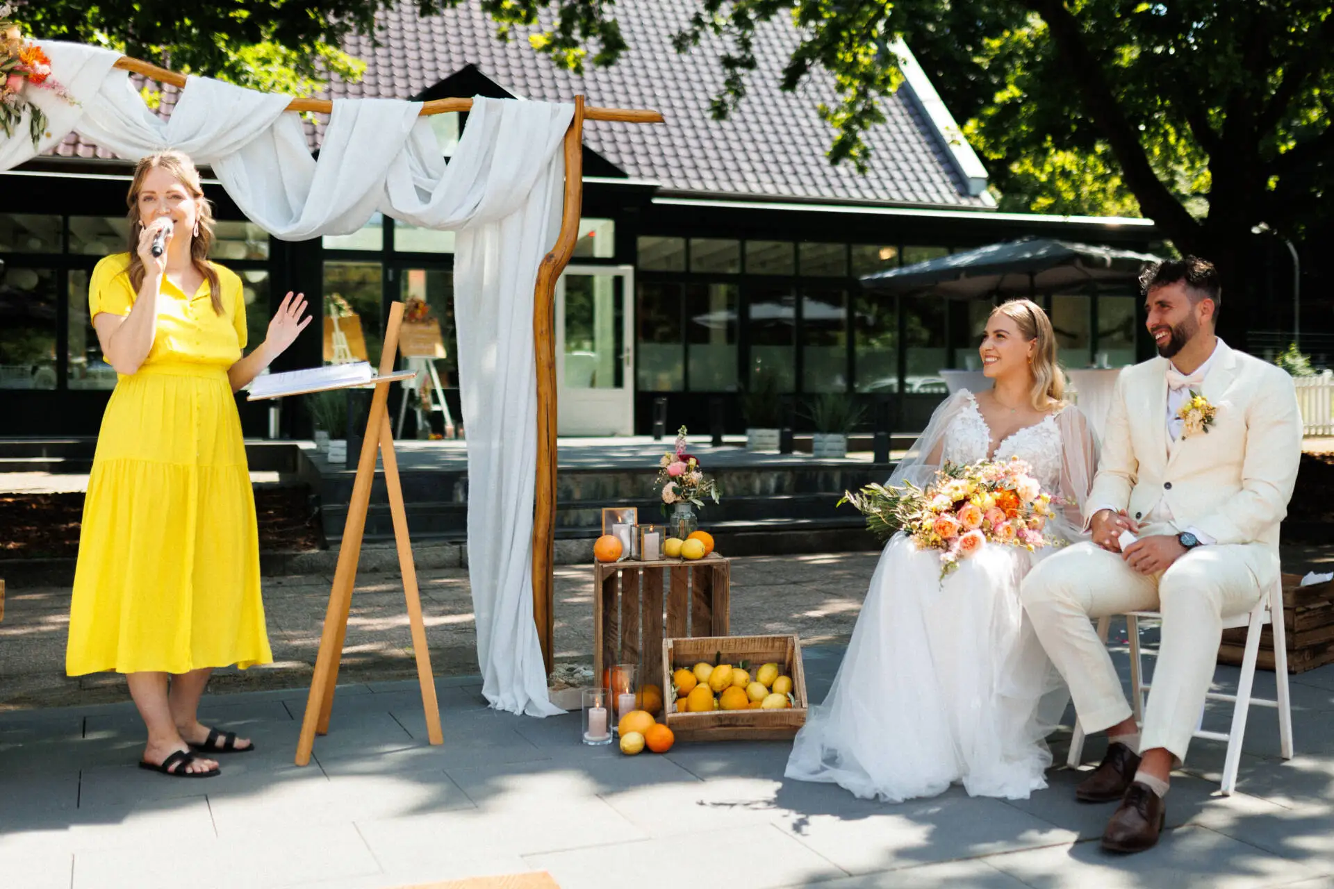Hochzeitszeremonie im Freien mit Brautpaar und Rednerin.