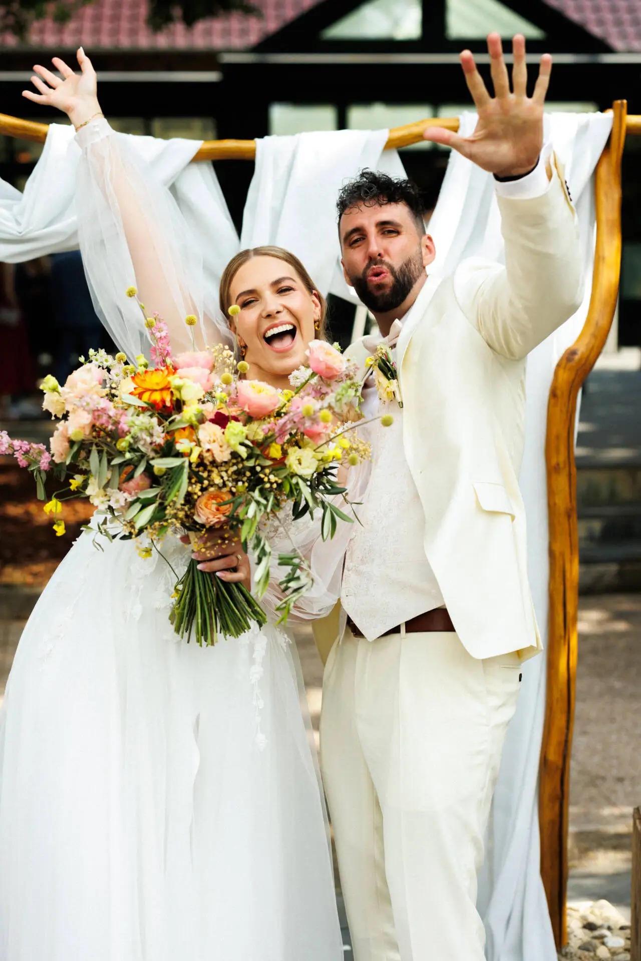 Glückliches Hochzeitspaar mit Blumenstrauß jubelt freudig.