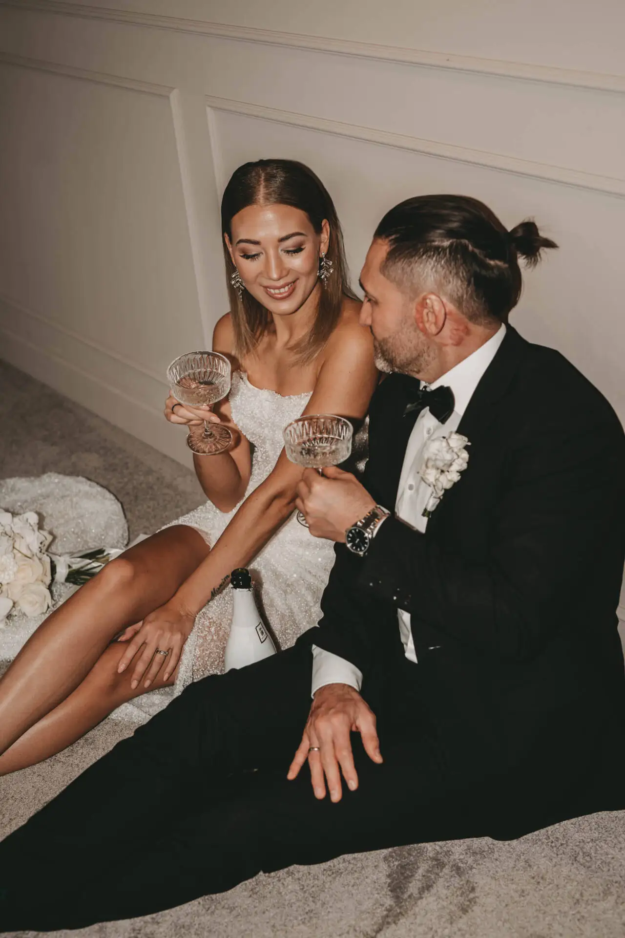 Brautpaar mit Champagnergläsern auf dem Boden sitzend.