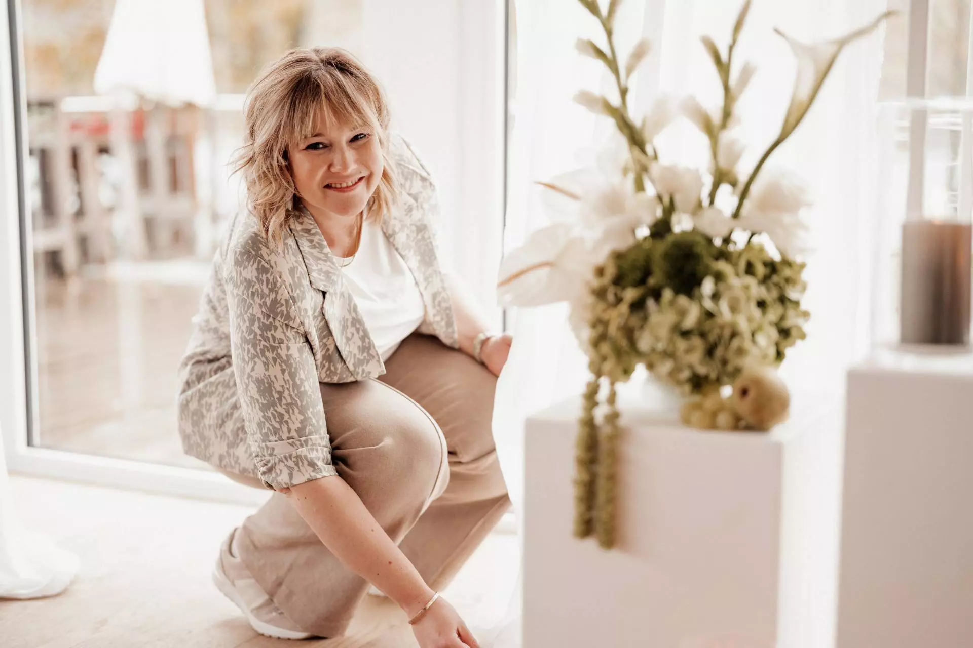 Frau lächelt neben Blume am Fenster