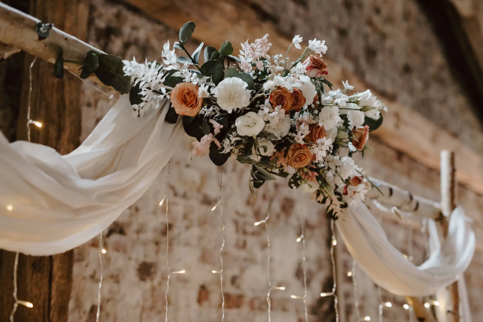 Blumengesteck mit Lichterkette und weißem Stoff