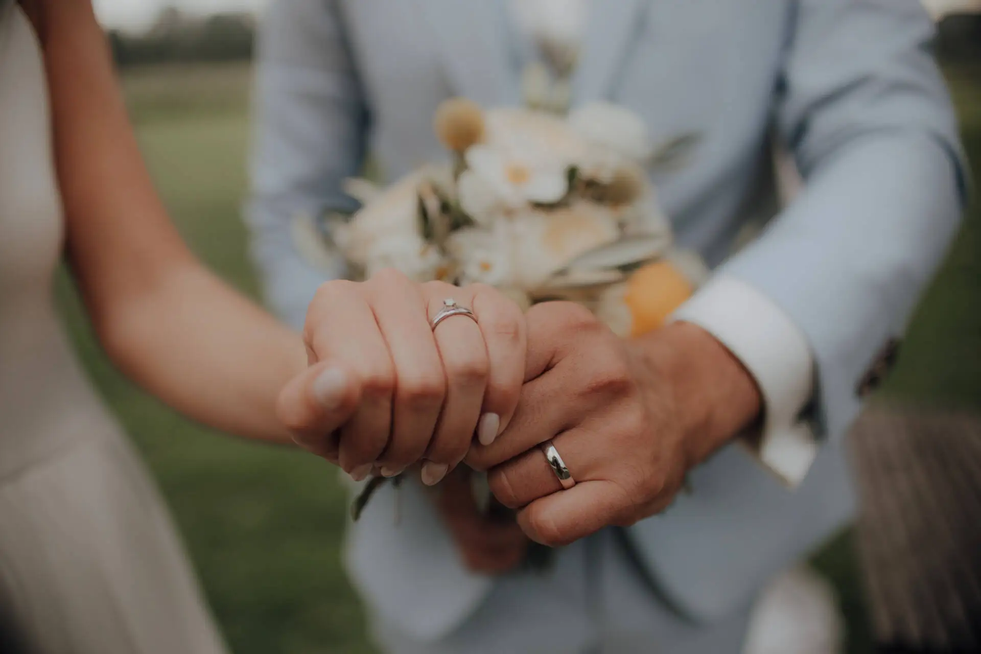 Eheringe an Paarhänden mit Blumenstrauß