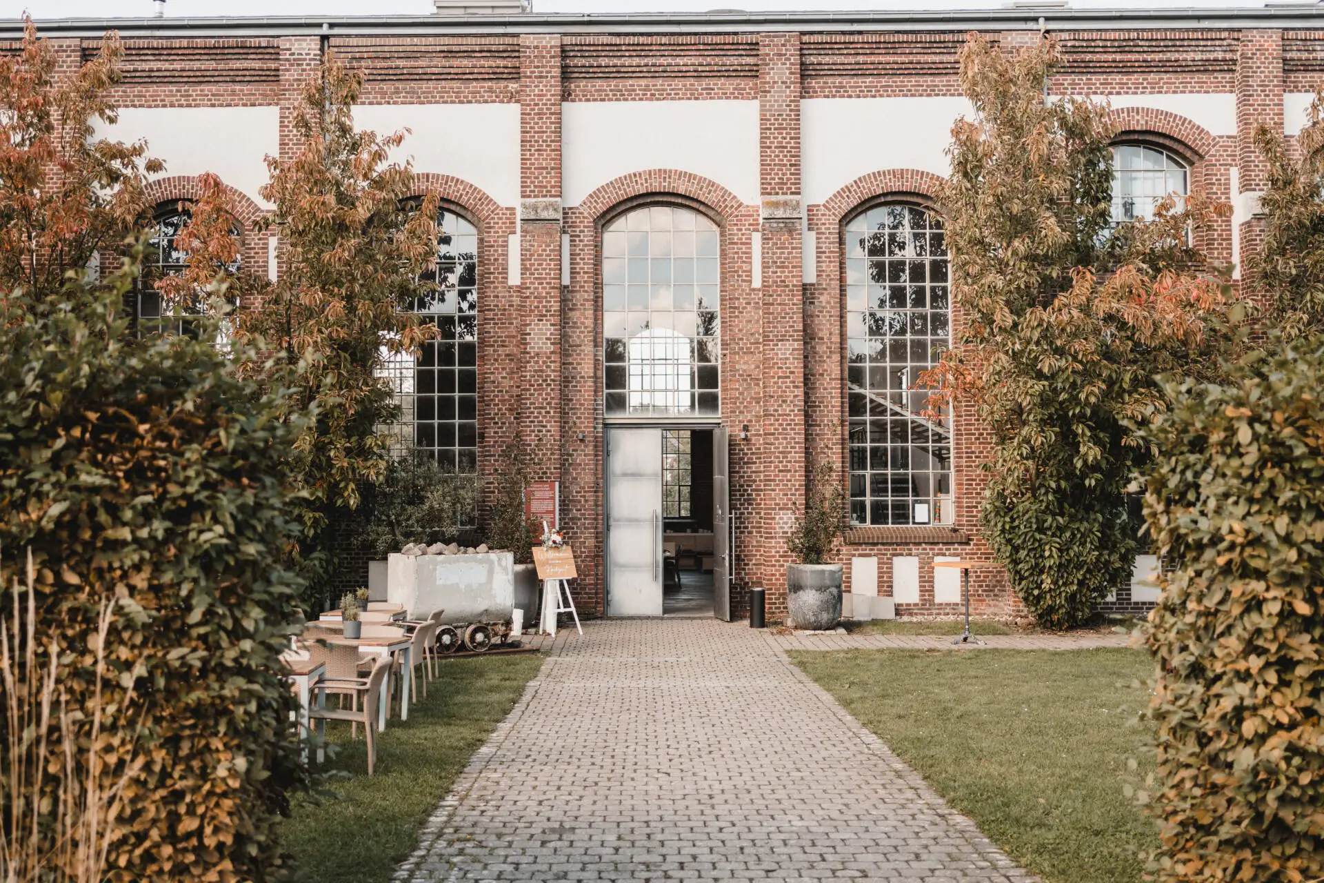 Historisches Backsteingebäude mit Bäumen und Stühlen.