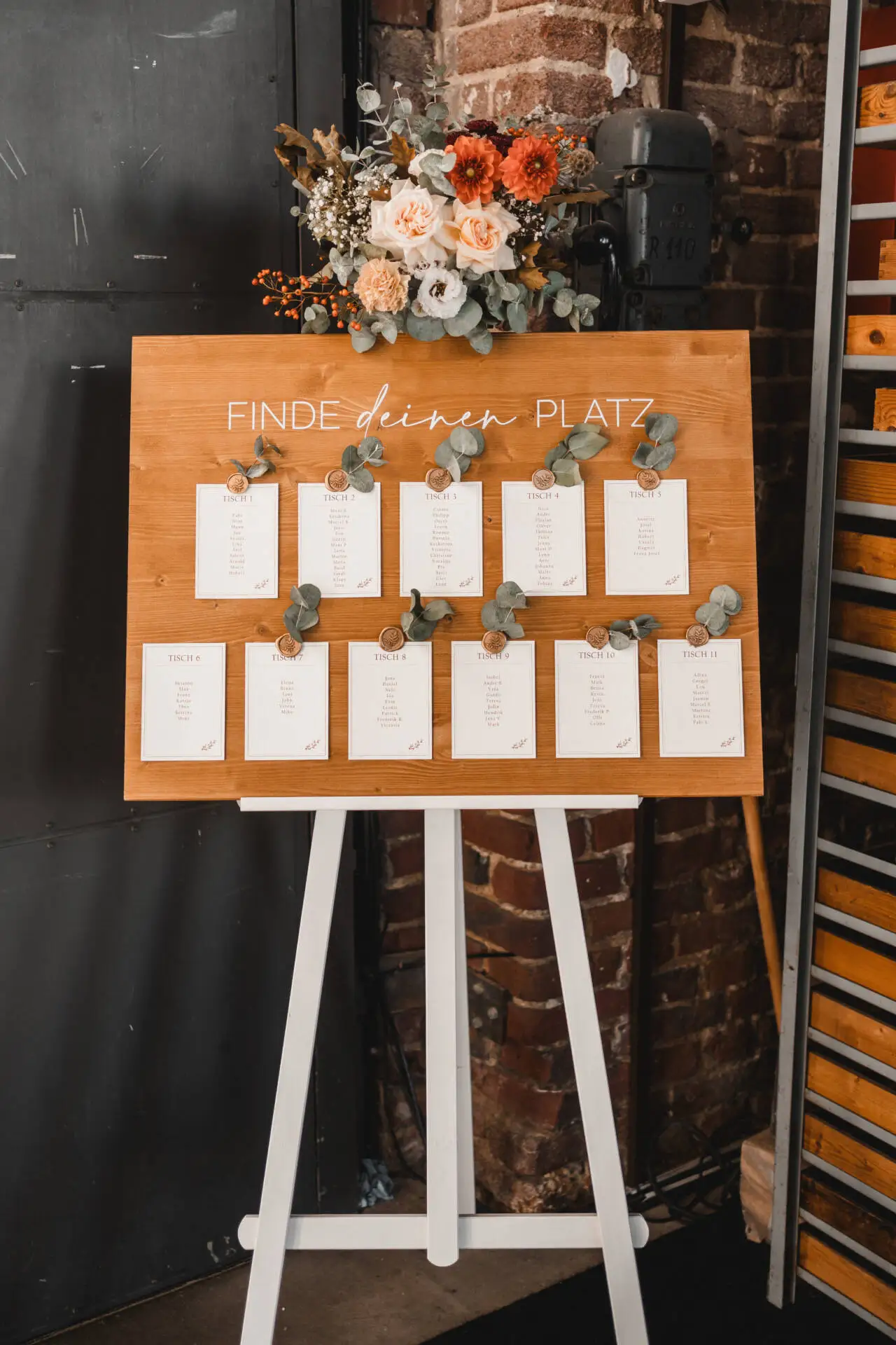 Hochzeits-Sitzplan auf Holztafel mit Blumendekoration.