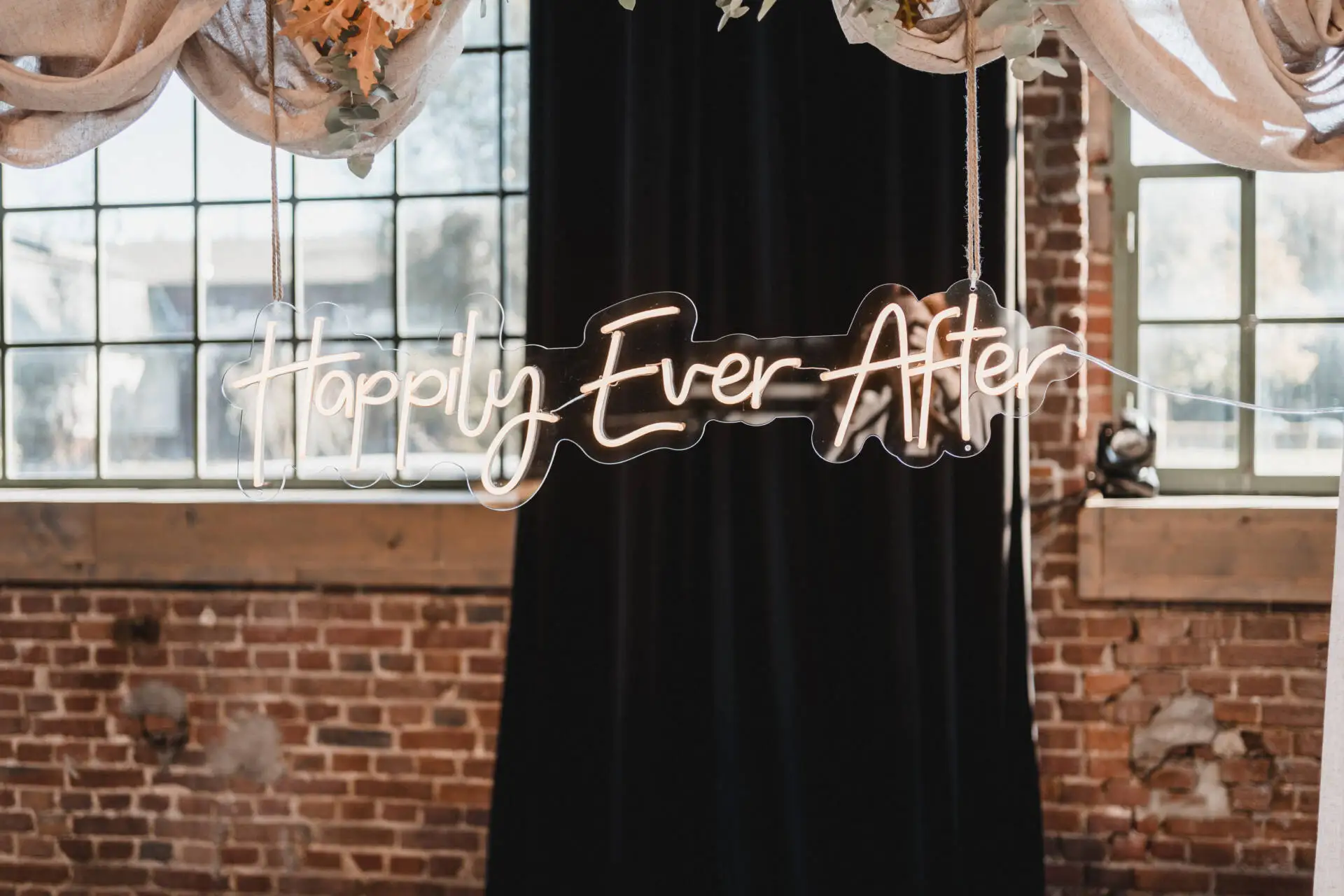 Leuchtschild 'Happily Ever After' vor Ziegelwand.