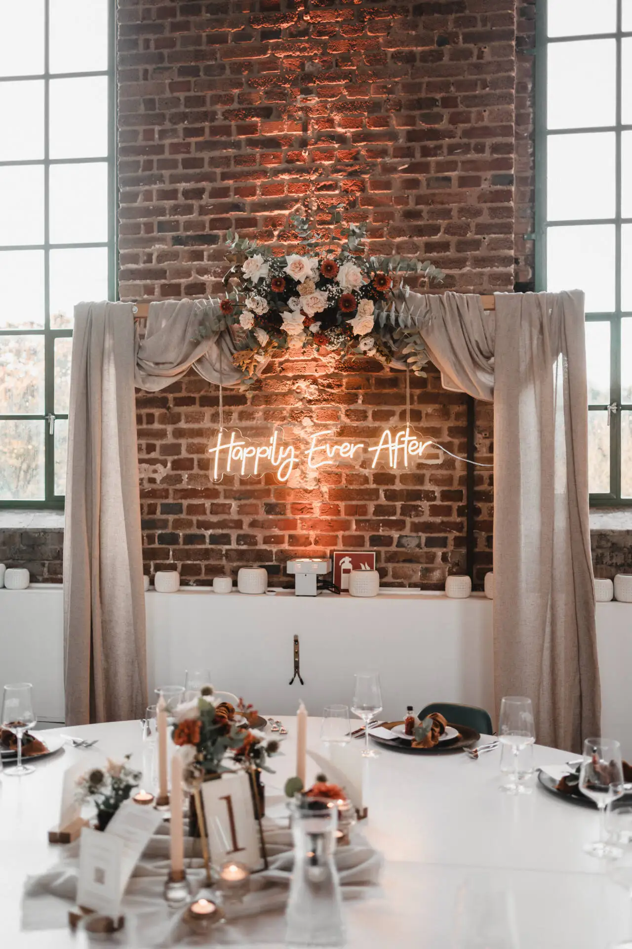 Hochzeitstischdekoration mit Blumen und Neonschriftzug.