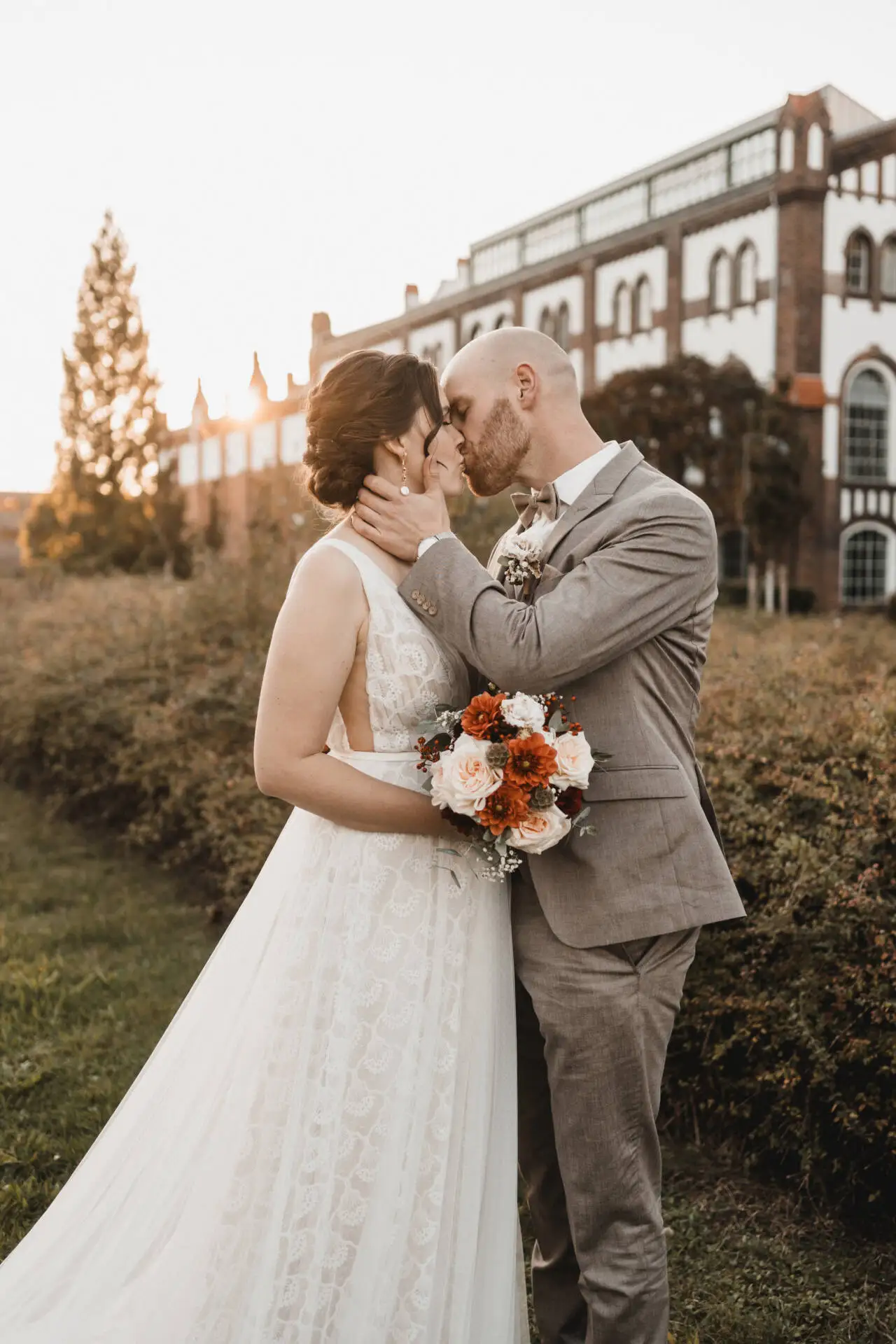Hochzeitspaar küsst sich im Garten vor Gebäude