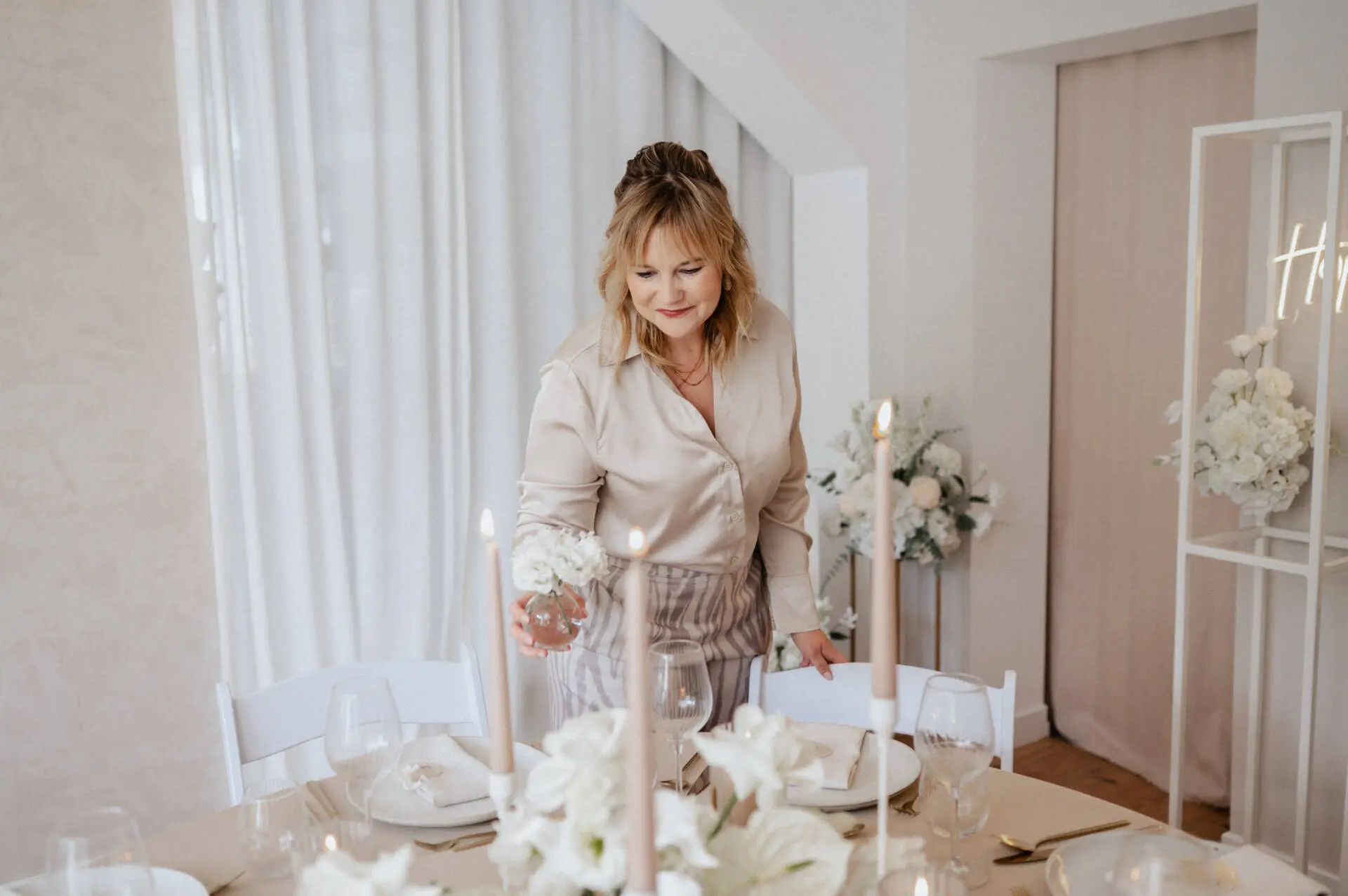 Frau dekoriert Tisch mit Kerzen und Blumen.