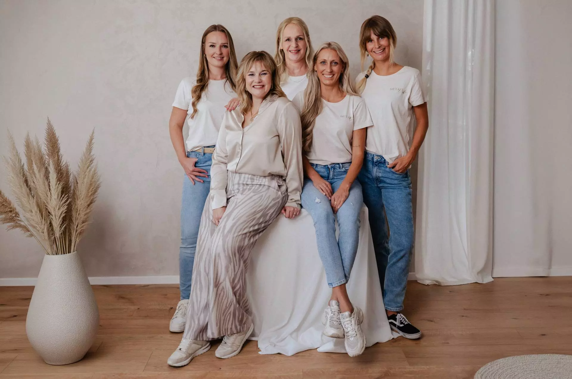 Fünf Frauen posieren vor beigem Hintergrund.