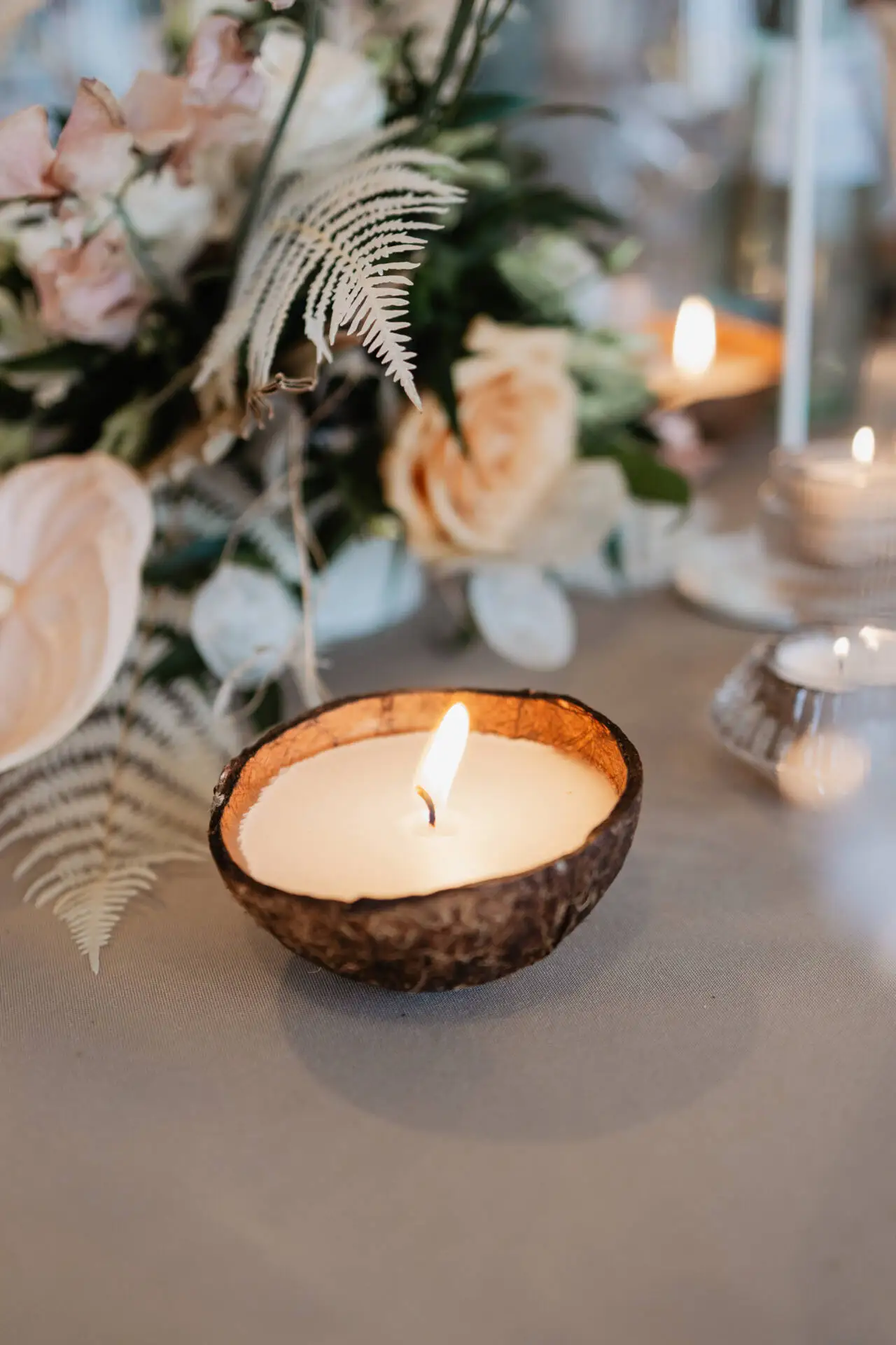 Brennende Kerze in Schale vor Blumenbouquet