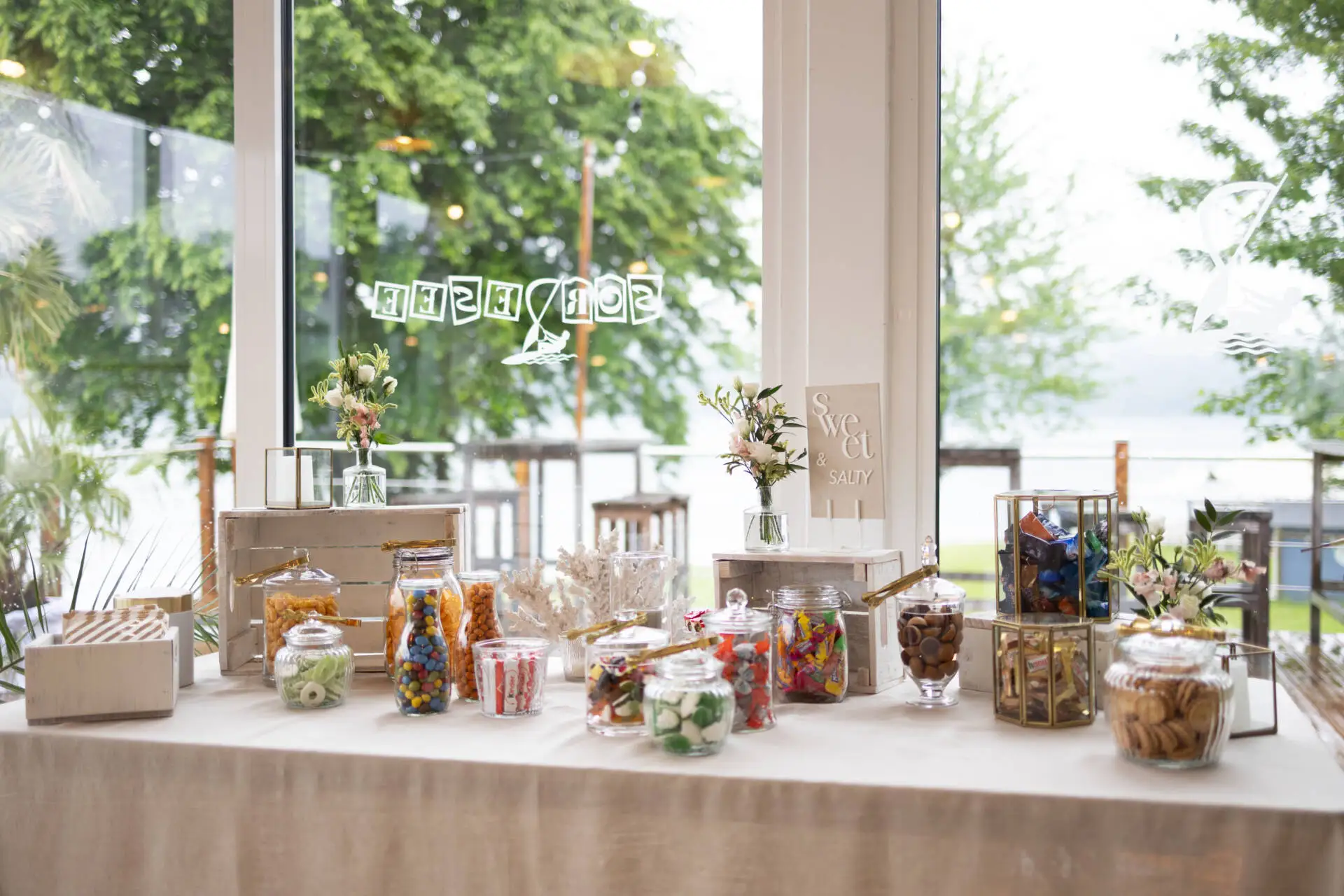 Süßigkeiten-Tisch mit Gläsern und Blumen dekoriert.