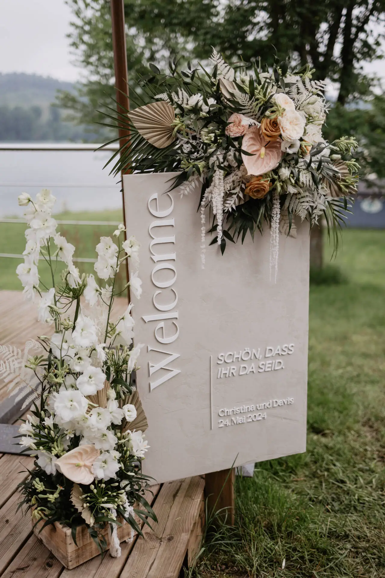 Willkommensschild mit Blumenarrangement auf Holzplattform