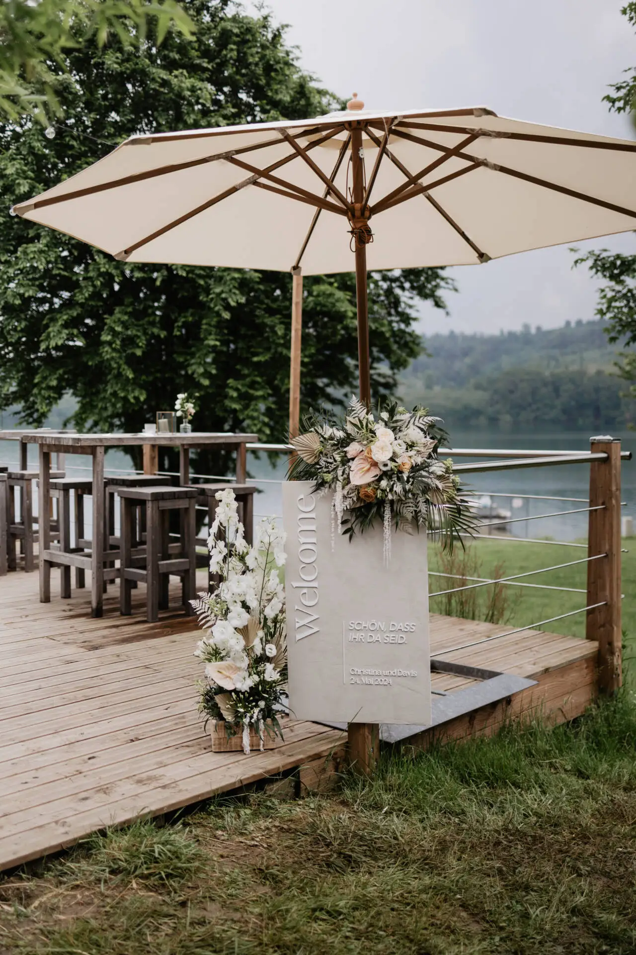 Hochzeitsdeko mit Blumen und Willkommensschild am See