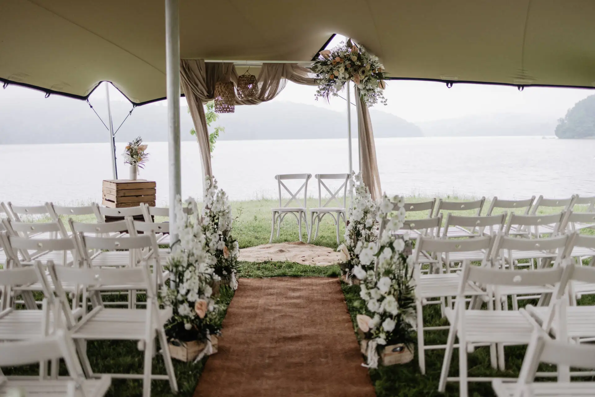 Romantische Hochzeitskulisse mit Stühlen und Blumen am Seeufer.